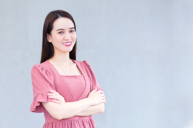 Une femme asiatique prospère qui porte du rose croise les bras et sourit joyeusement au bureau.