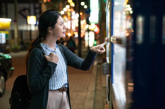 femme asiatique à la recherche de quoi boire. debout devant un distributeur automatique.