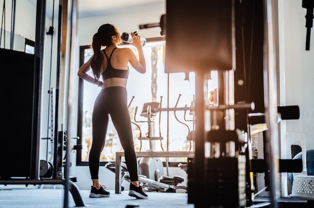 Femme asiatique de remise en forme se détendre après avoir exercé ses eaux potables à la salle de sport