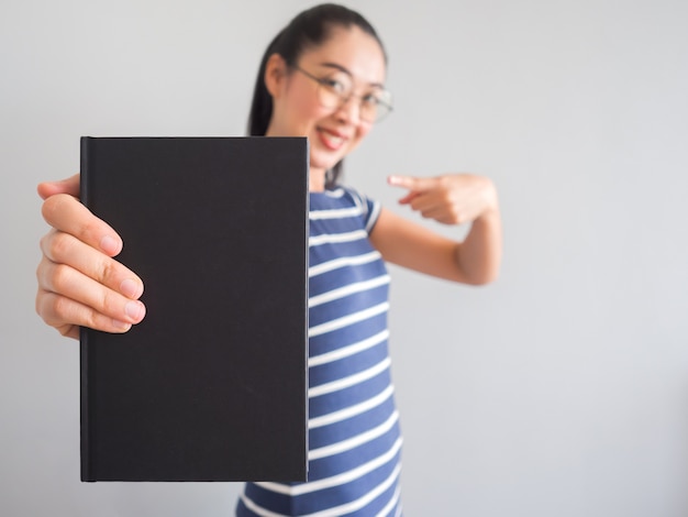 Une femme asiatique ringarde sourit et tient un bon livre.