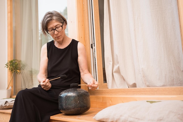 Femme asiatique en robe noire assise sur la terrasse d'une maison de campagne avec bol chantant