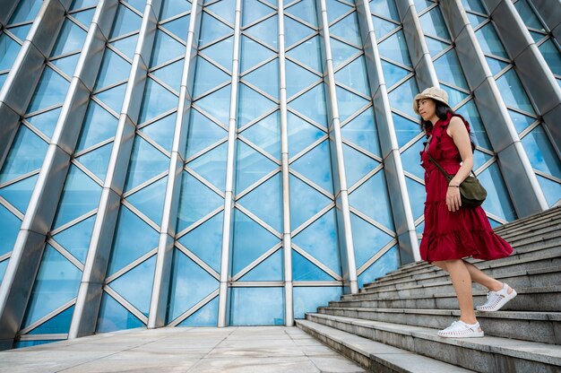 Femme asiatique en robe rouge au bâtiment moderne, fille de sexe féminin avec mode de vie urbain