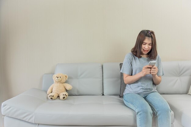 Une femme asiatique s'assoit sur un canapé utilise un téléphone intelligent vérifie les e-mails fille asiatique regarde les médias sociaux mobiles