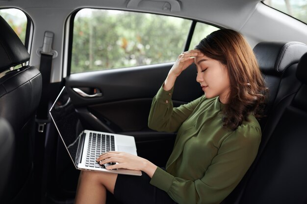 Une femme asiatique s'ennuie au travail avec un ordinateur portable alors qu'elle est assise dans sa voiture