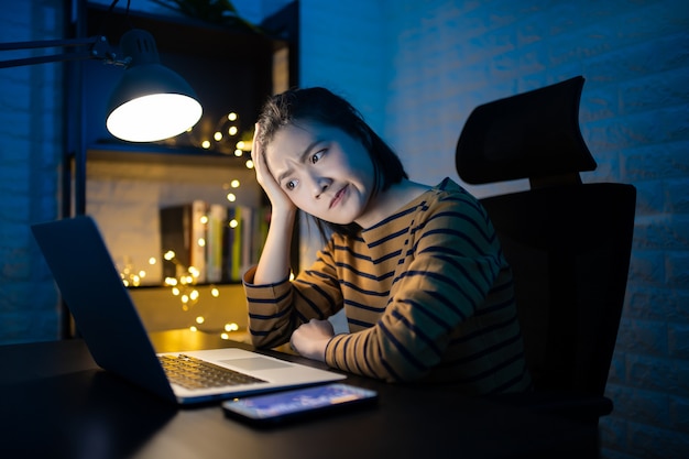 Femme asiatique s'ennuie de travailler sur un ordinateur portable à la maison. . Travaillez à domicile pour éviter le concept Coronavirus COVID 19.