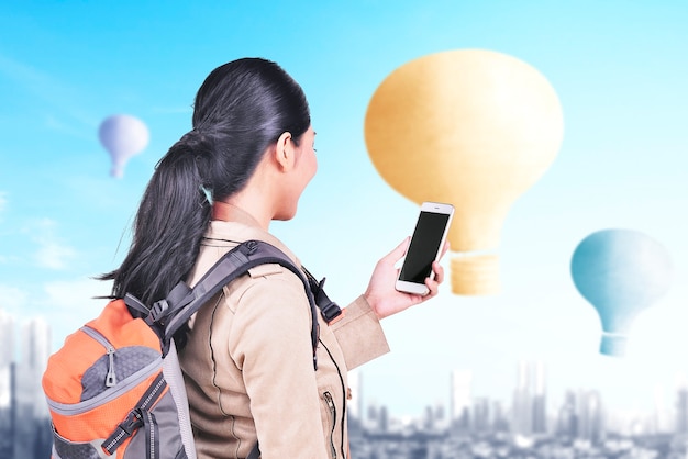 Femme asiatique avec sac à dos et smartphone regardant un ballon à air coloré volant avec un fond de paysage urbain