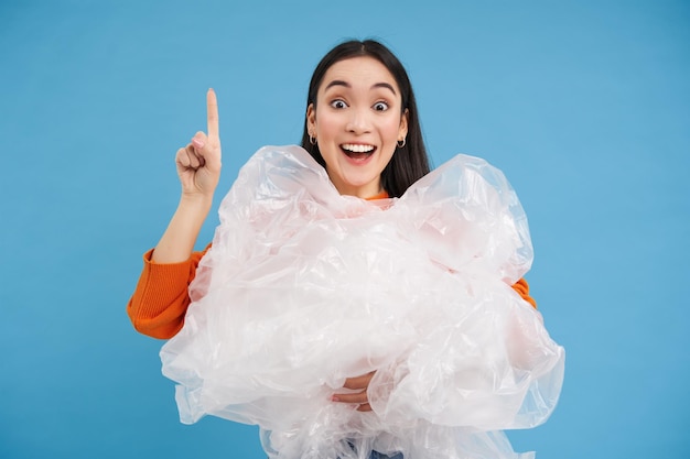 Femme asiatique avec des sacs en plastique recyclage des déchets dans les mains pointe vers le haut montrant recycler le centre de tri sust