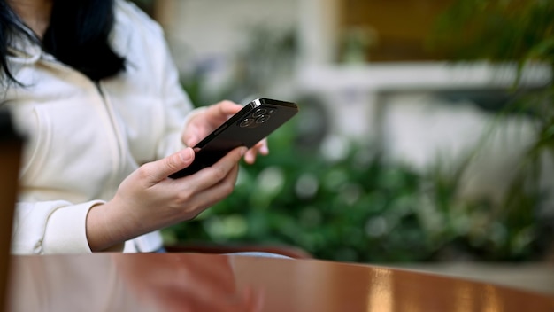 Une femme asiatique se détend assise à l'espace extérieur du café et utilise son smartphone