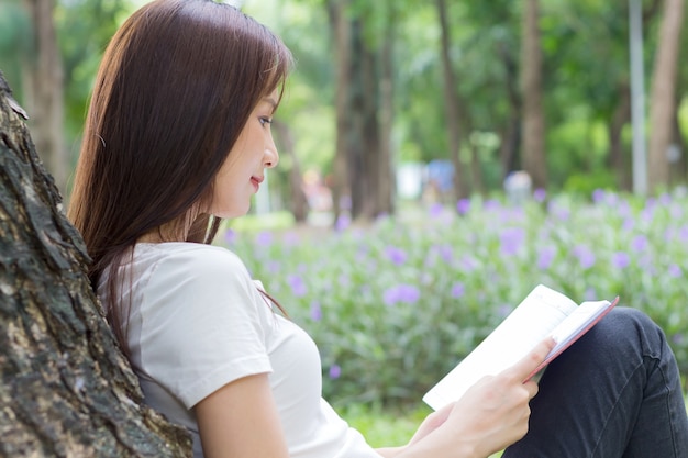 Femme asiatique se détendre en assis joyeusement en lisant un livre dans le parc