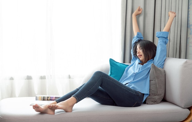 Une femme asiatique se réveille après avoir dormi et se détend sur un canapé-lit dans son salon dans sa copropriété