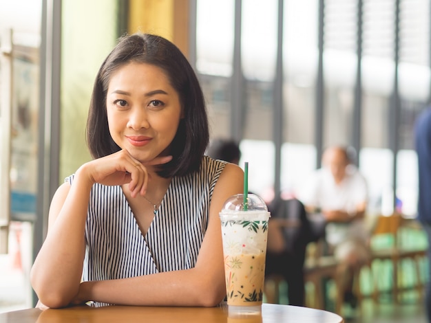 Femme asiatique se trouve au café café avec café glacé sur la table.