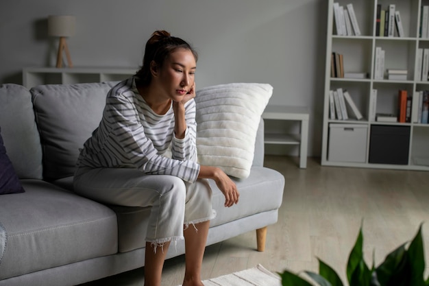 Photo femme asiatique solitaire en détresse inquiète confuse assise sur le canapé à la maison femme souffrant de problèmes de santé mentale