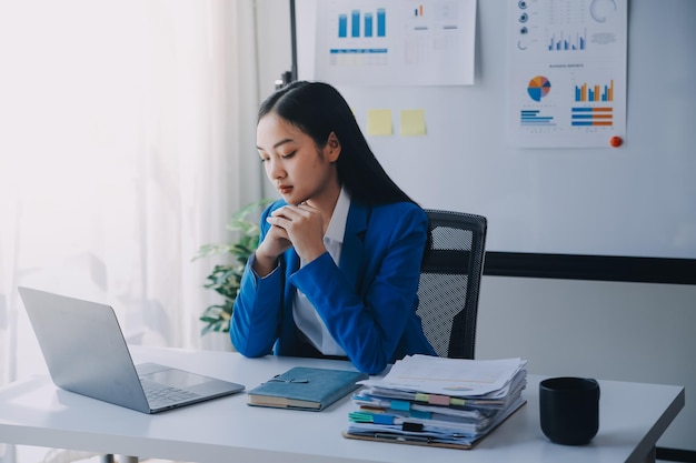 Photo une femme asiatique souffrant de migraines, de tensions cérébrales, d'une femme d'affaires surchargée de travail, d'un financier travaillant sur un ordinateur portable et une tablette dans un bureau moderne.