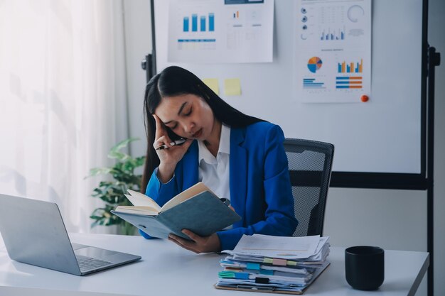 Photo une femme asiatique souffrant de migraines, de tensions cérébrales, d'une femme d'affaires surchargée de travail, d'un financier travaillant sur un ordinateur portable et une tablette dans un bureau moderne.