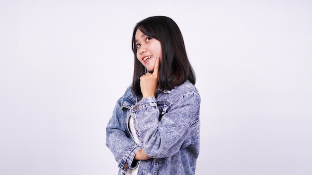 Femme asiatique souriant portant une veste en jean et en pensant à une idée avec une surface blanche isolée