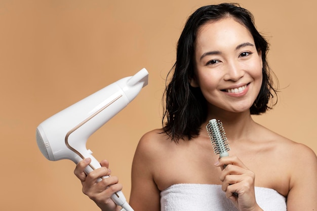 Femme asiatique souriante à l'aide d'un sèche-cheveux sur fond de studio beige