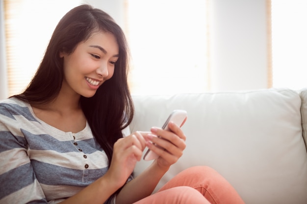 Femme asiatique souriante sur le canapé à l&#39;aide de téléphone