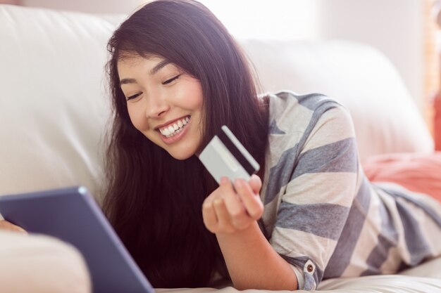 Femme asiatique souriante sur canapé avec tablette pour magasiner en ligne à la maison dans le salon