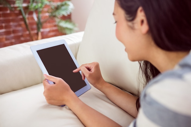 Femme asiatique souriante sur le canapé avec tablette