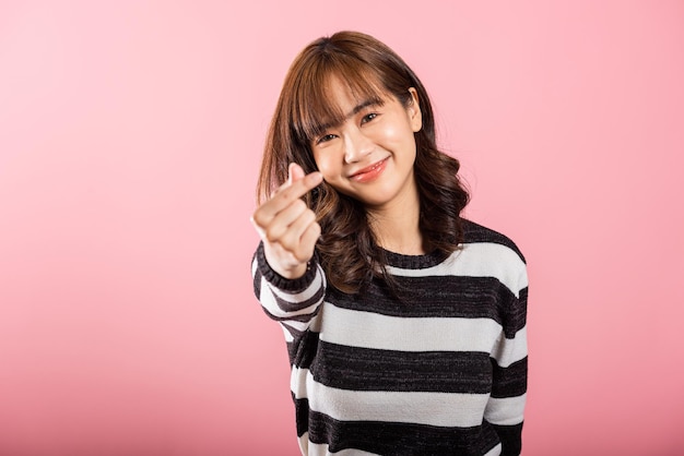 Une femme asiatique souriante dégage de la confiance en présentant un mini signe de cœur avec son doigt sur un fond rose Portrait d'une belle jeune femme envoyant de l'amour pour la Saint-Valentin dans un tournage de studio