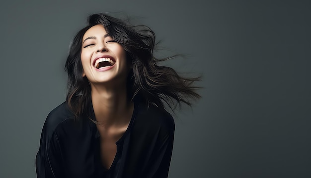 Une femme asiatique souriante avec du vent dans ses cheveux noirs en studio.