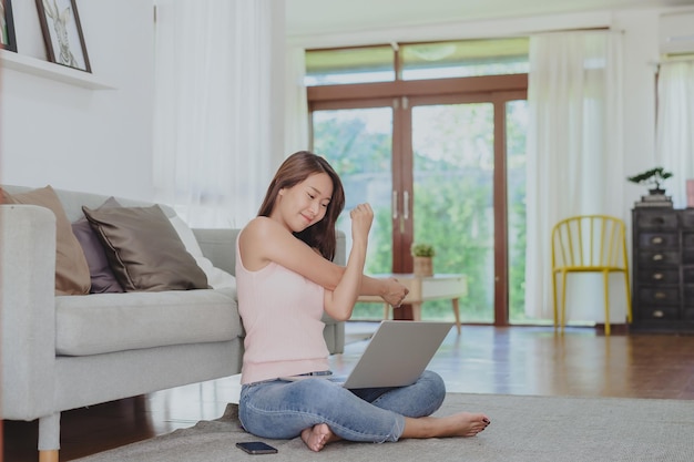 Femme asiatique souriante étirant son épaule pour se détendre après avoir travaillé à domicile via un ordinateur portable