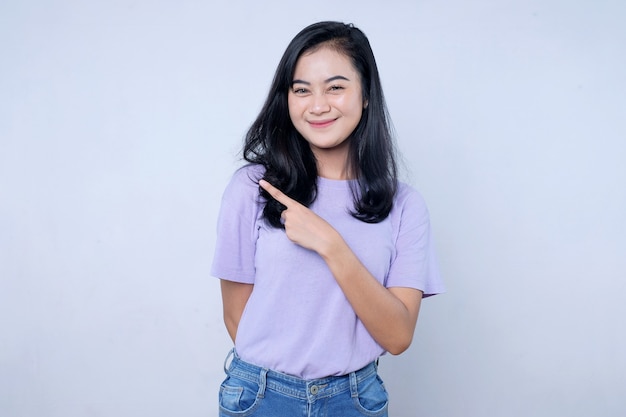 Femme asiatique souriante et heureuse avec son doigt gauche pointé et isolée sur fond de bannière blanc clair avec espace de copie