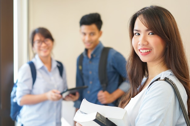 femme asiatique souriante et portant des manuels scolaires avec des amis au campus de l&#39;Université