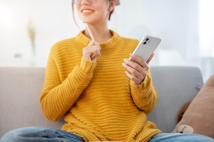 Photo une femme asiatique souriante et positive réfléchissant à des idées tout en utilisant son smartphone sur un canapé à la maison