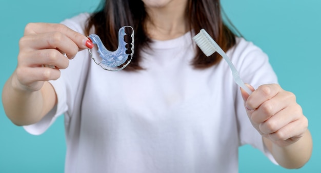 Femme Asiatique Souriante Tenant Un Appareil De Rétention Orthodontique Sur Fond D'écran Bleu. Soins Dentaires Et Dents Saines.