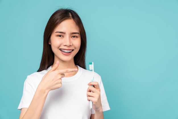 Femme asiatique souriante tenant une brosse à dents avec des accolades sur les dents isolées sur fond bleu Concept d'hygiène bucco-dentaire et de soins de santé