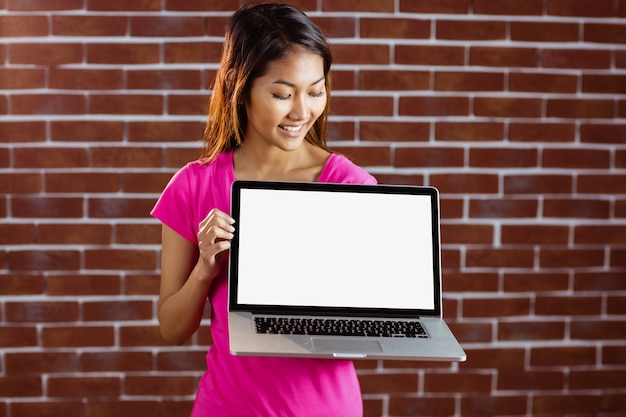 Femme asiatique souriante tenant l'ordinateur sur le mur de briques