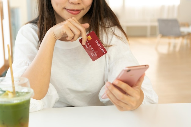 Femme asiatique souriante utilisant un téléphone portable tout en tenant une carte de crédit sur sa main dans un café Technologie et mode de vie Concept de société sans numéraire Gros plan