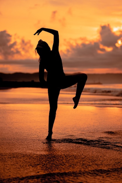 Une femme asiatique sous forme de silhouette faisant des mouvements de ballet très agiles sur la plage