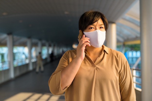 Femme asiatique en surpoids avec masque parlant au téléphone dans la ville