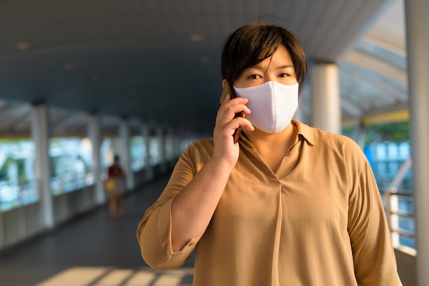 Femme asiatique en surpoids avec masque parlant au téléphone dans la ville