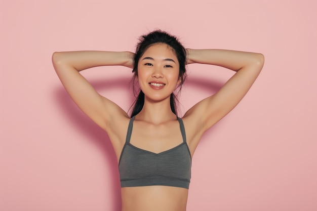 Une femme asiatique en T-shirt blanc a mis ses mains derrière sa tête contre un fond de studio rose clair.