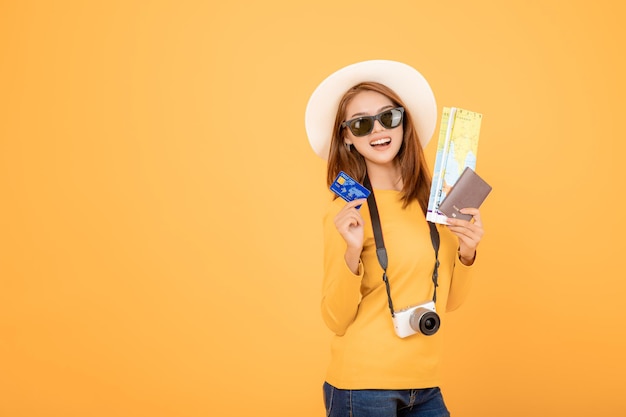 Photo une femme asiatique tenant une carte de crédit, une carte et un passeport, un concept de voyageur avec une caméra sur fond jaune.