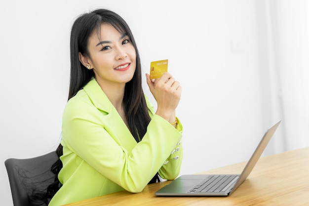 Femme asiatique tenant une carte de crédit d'entreprise bancaire avec un ordinateur portable