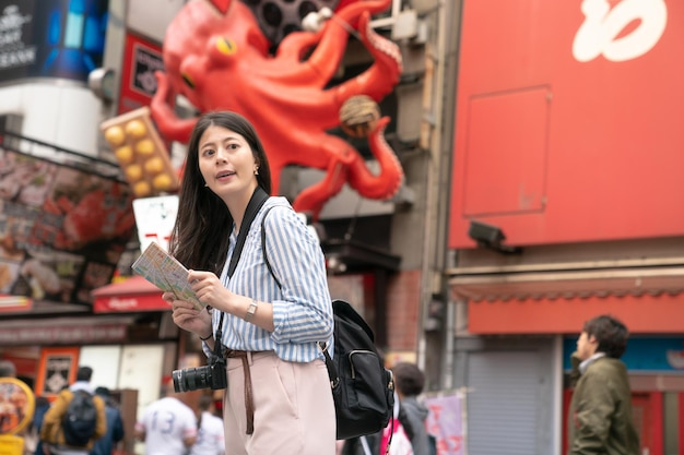 femme asiatique tenant une carte et à la recherche d'un endroit. regardant joyeusement et confortable. vue de côté.