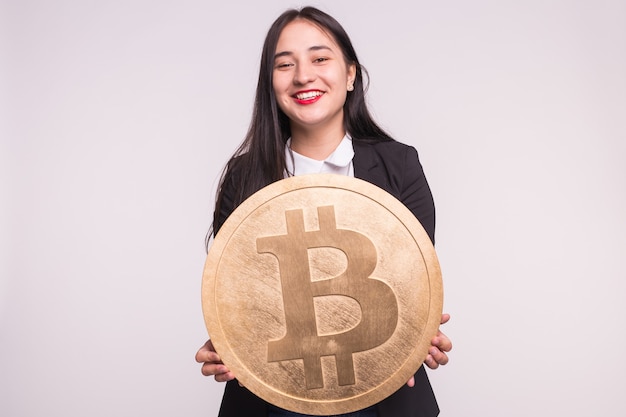 Femme asiatique tenant gros bitcoin sur mur blanc. Concept d'investissement de crypto-monnaie.