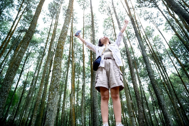 Une femme asiatique tenant un téléphone portable avec une expression heureuse dans la forêt