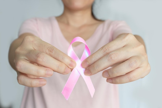Une femme asiatique tient un ruban rose à la main pour encourager une patiente atteinte d'un cancer du sein et soutenir la campagne contre le cancer du sein en octobre