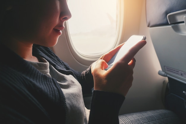 Femme asiatique touristique assis près de la fenêtre de l&#39;avion et utilisant un téléphone intelligent pendant le vol.