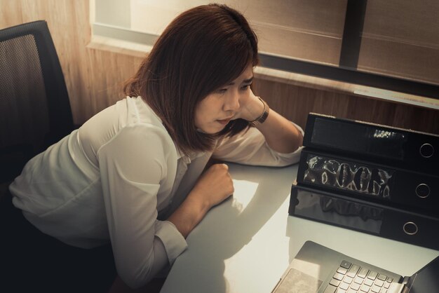Femme asiatique travaillant au bureaujeune femme d'affaires stressée par la surcharge de travail avec beaucoup de fichiers sur le bureau