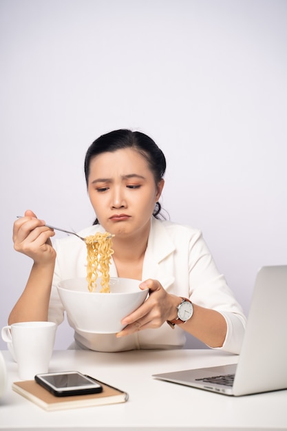 Femme asiatique travaillant dur des heures supplémentaires en mangeant des nouilles instantanées au bureau. Femme d'affaires bouleversée surmenée occupée et affamée.