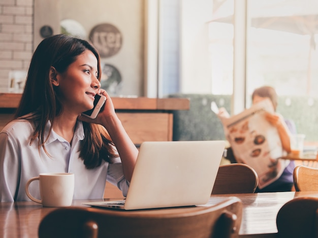 Femme asiatique travaillant avec ordinateur portable dans un café.