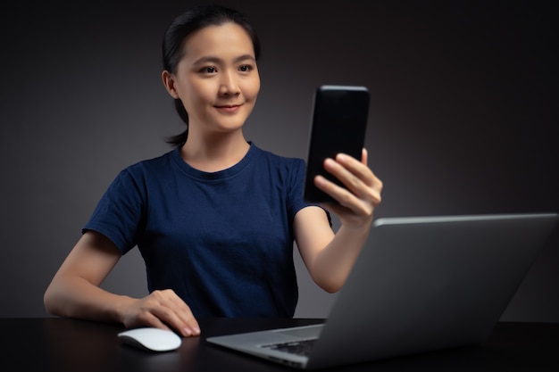 Femme asiatique travaillant sur un ordinateur portable scanne le visage par smartphone à l'aide du système de reconnaissance faciale.