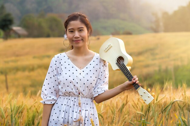 Femme asiatique avec ukulélé dans le champ d&#39;orge au coucher du soleil