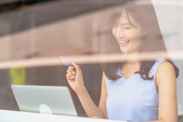 Femme asiatique utilisant une carte de crédit avec un téléphone portable et un ordinateur portable technologique pour les achats en ligne